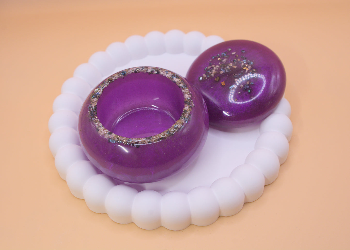 A handmade trinket pot, displayed on a white tray, the lid is off to the side of the pot, showing cremation ashes and sparkle shards around the rim