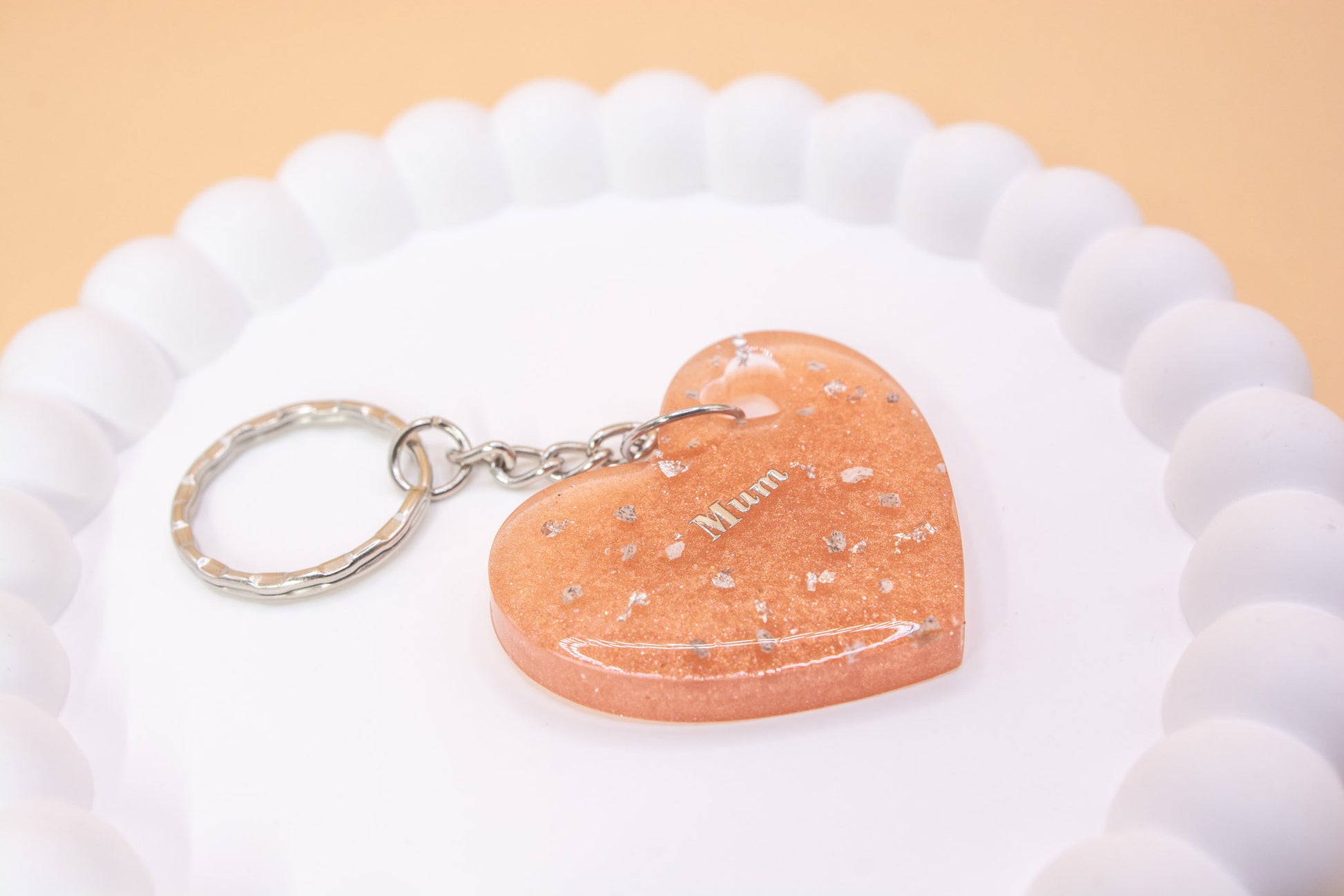 Alternative close up view of a heart shape keyring containing cremation ashes with the word "Mum" on it, presented on a display tray