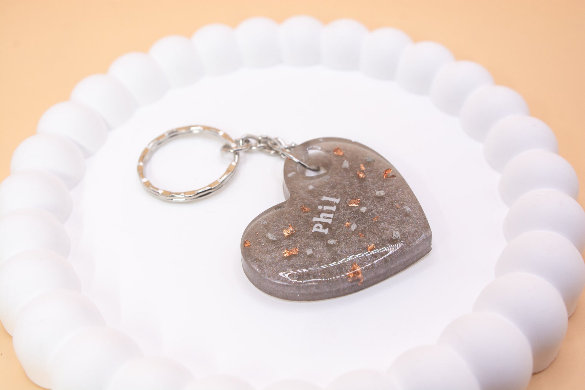 A Gunmetal Grey heart shaped keyring containing cremation ashes with the name Phil on it, presented on a display tray side view