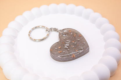 A Gunmetal Grey heart shaped keyring containing cremation ashes with the name Phil on it, presented on a display tray side view