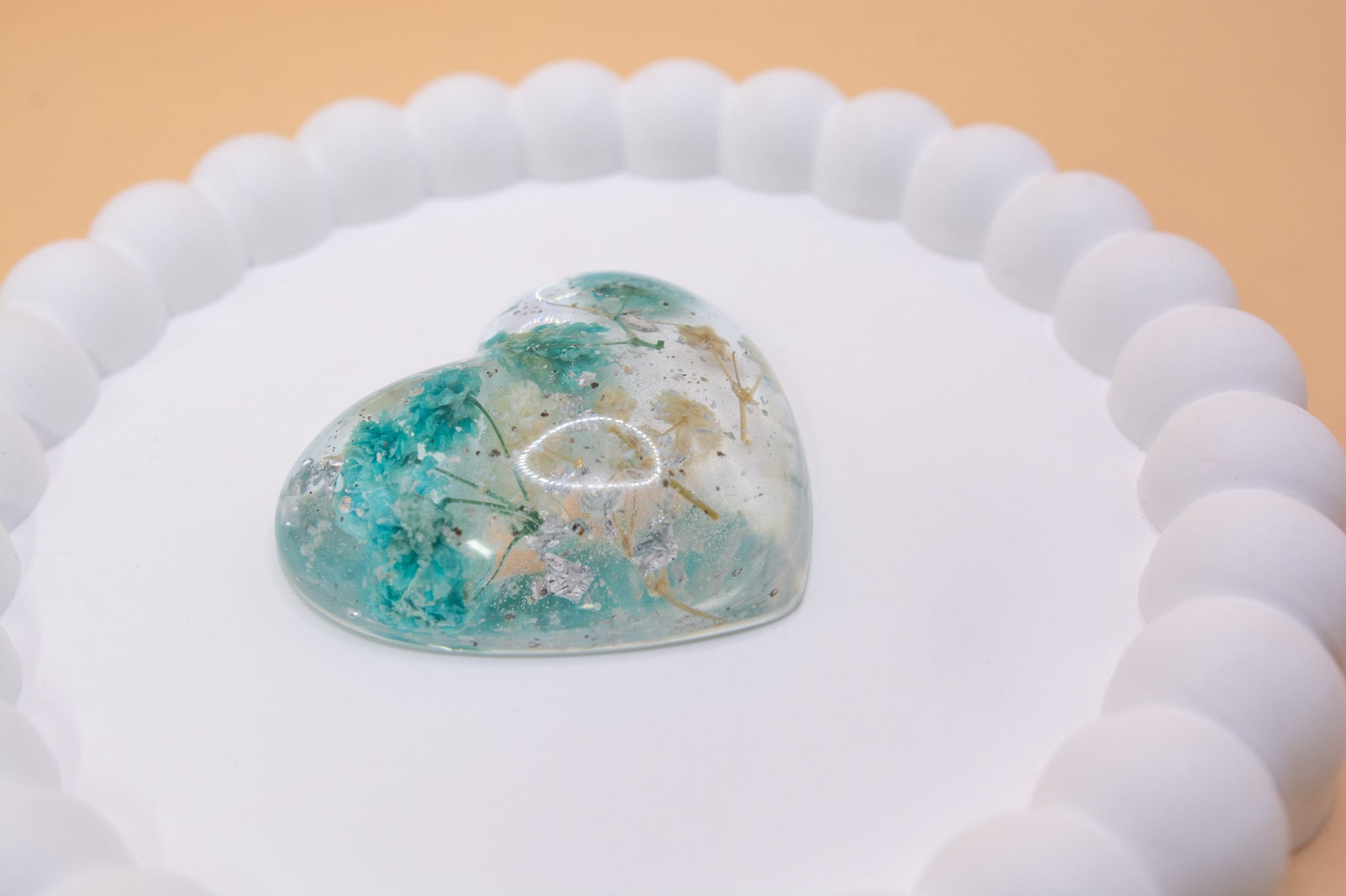 A heart shaped cremation ashes ornament, containing blue and cream dried flowers and silver flakes, presented on a display tray