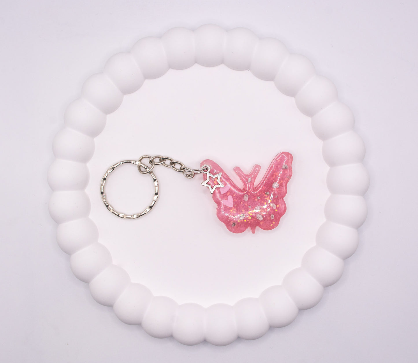 An aerial over head head view of a Pink butterfly keepsake memorial keyring, containing cremation ashes and glitter, set on a silver keychain, presented on a display tray
