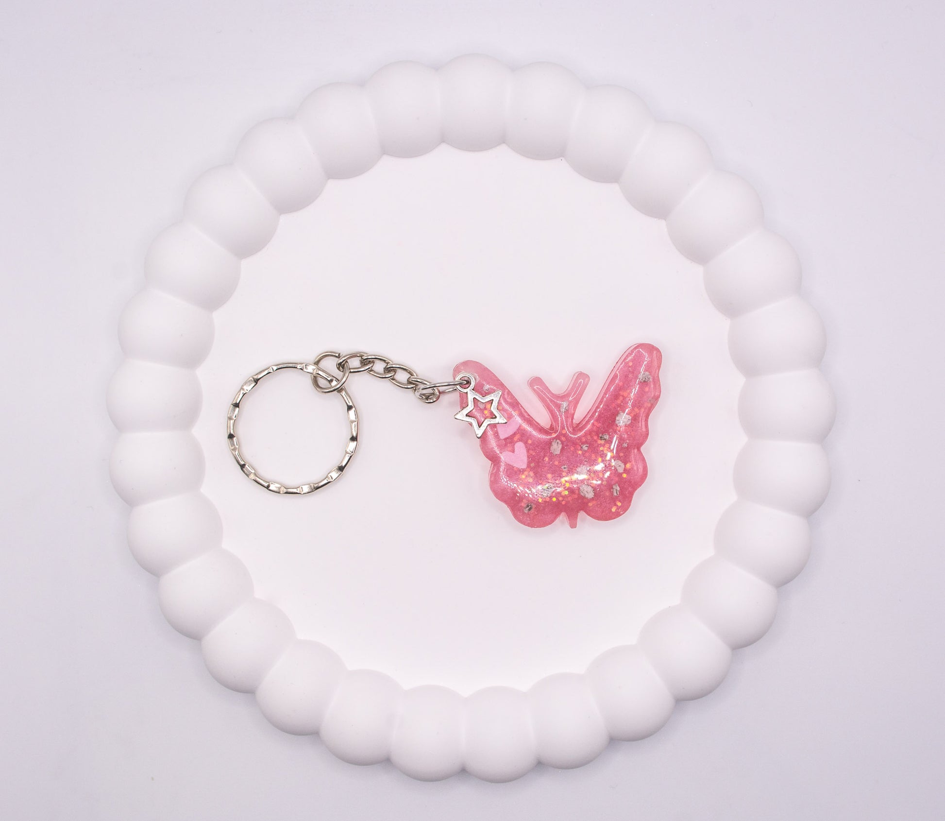 An aerial over head head view of a Pink butterfly keepsake memorial keyring, containing cremation ashes and glitter, set on a silver keychain, presented on a display tray