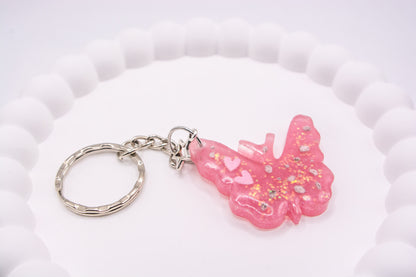 Close up angled view of a Pink butterfly keepsake memorial keyring, containing cremation ashes and glitter, set on a silver keychain