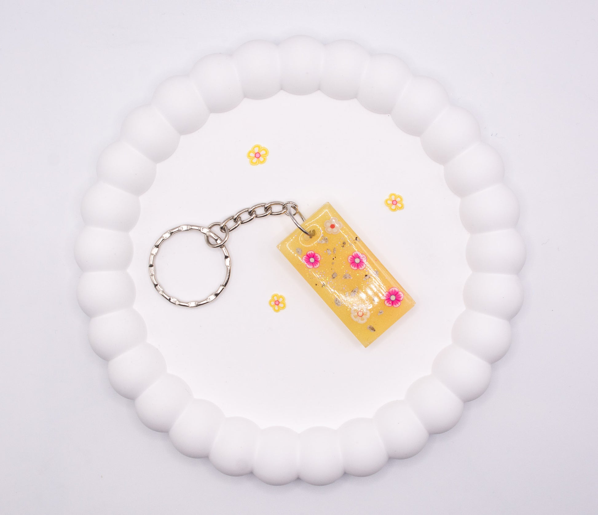 Over head view of a yellow rectangle keepsake memorial keyring, containing flower decorations and cremation ashes, set on a silver keychain
