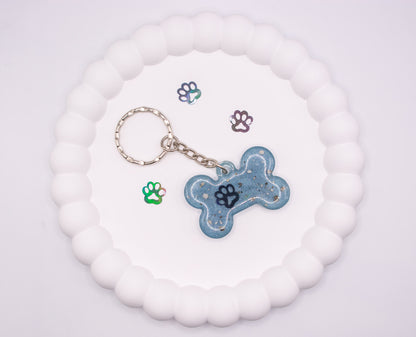 An aerial, overhead view of a light blue bone shaped keepsake memorial keyring, containing pet cremation ashes, set on a silver keychain