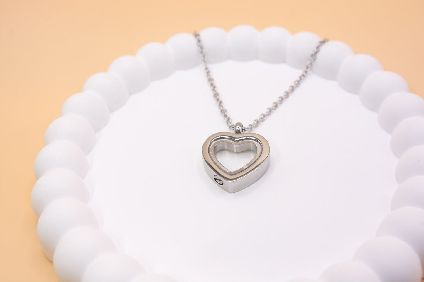 An alternative view of a stainless steel heart pendant, showing the bottom, where you can be self-fill the pendant with cremation ashes or sand from a favourite beach, it has a clear central window so you can see the contents