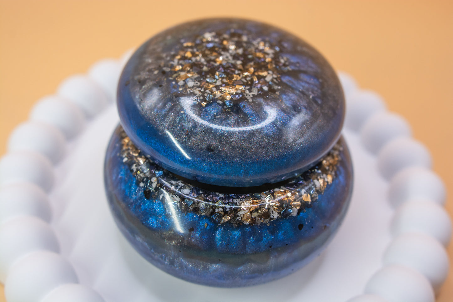A close up view of a metallic blue and grey handcrafted trinket pot, which contains gold sparkle fragments and cremation ashes