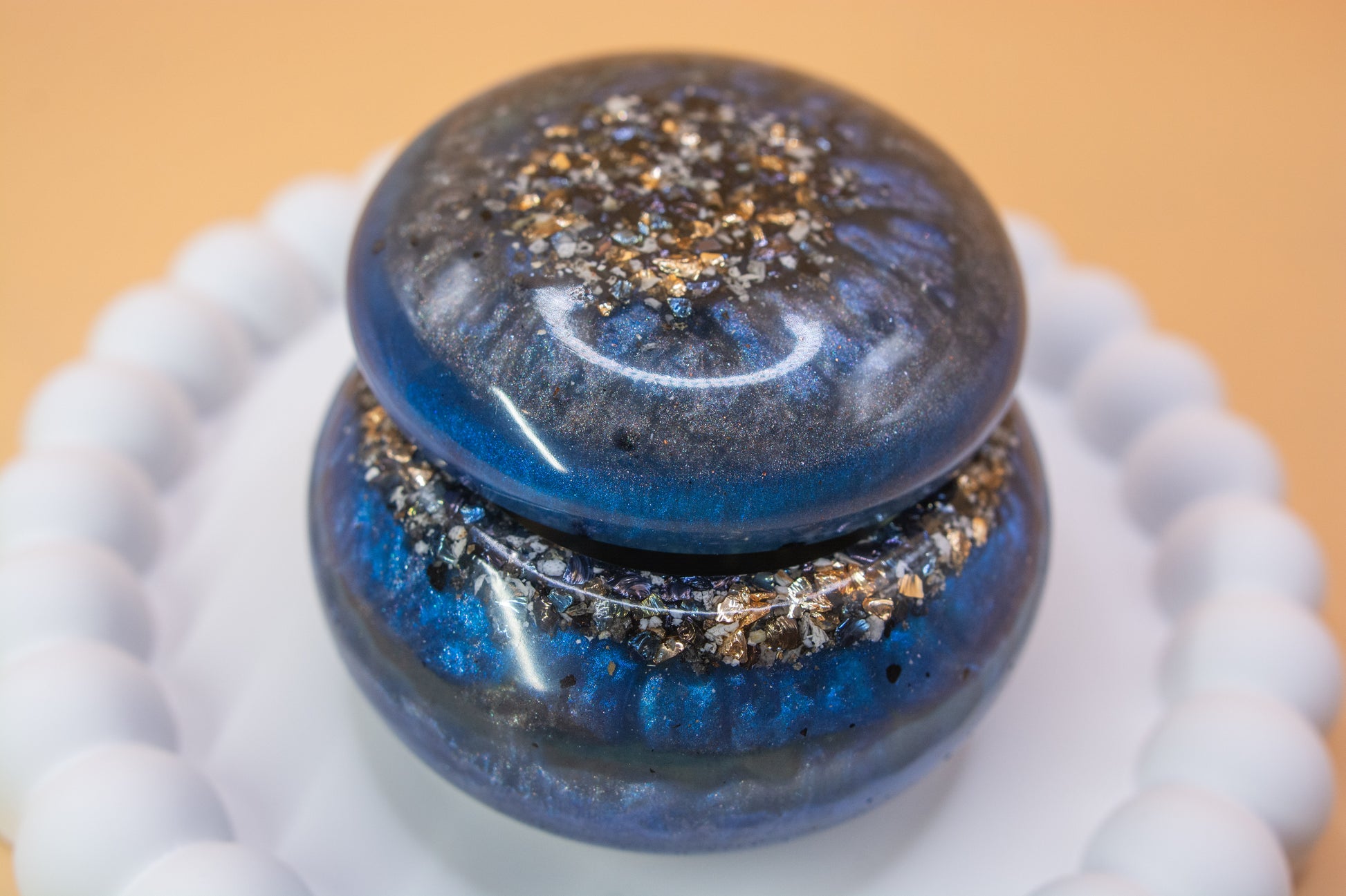 A close up view of a metallic blue and grey handcrafted trinket pot, which contains gold sparkle fragments and cremation ashes