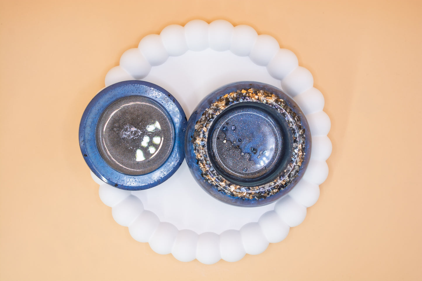 An overhead view of a metallic blue and grey handmade trinket pot, which has gold sparkle fragment and cremation ashes in it, the lid is to the side of the pot A front view of a metallic blue and grey handmade trinket pot, which has gold sparkle fragment 