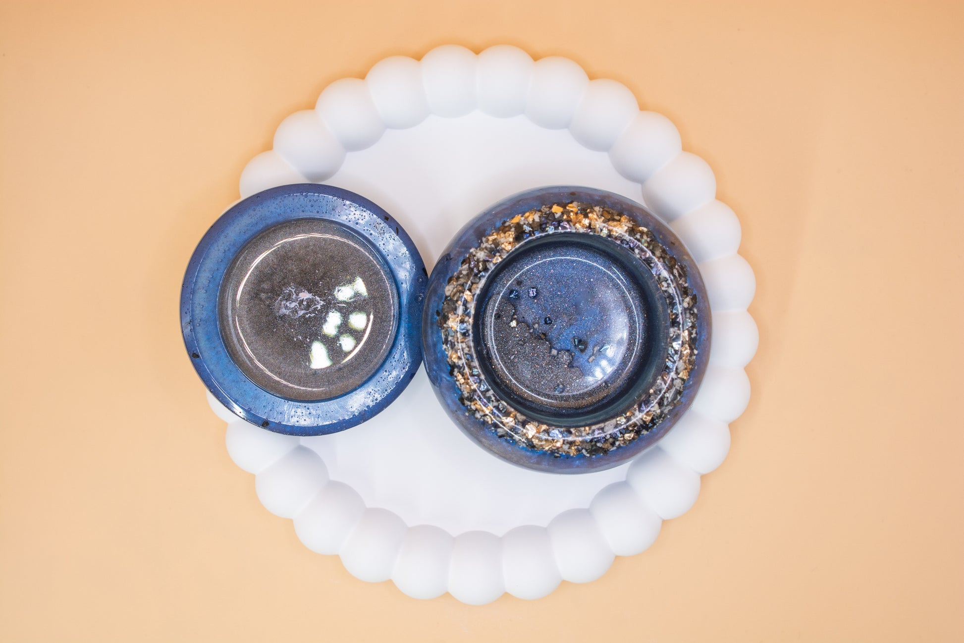 An overhead view of a metallic blue and grey handmade trinket pot, which has gold sparkle fragment and cremation ashes in it, the lid is to the side of the pot A front view of a metallic blue and grey handmade trinket pot, which has gold sparkle fragment 