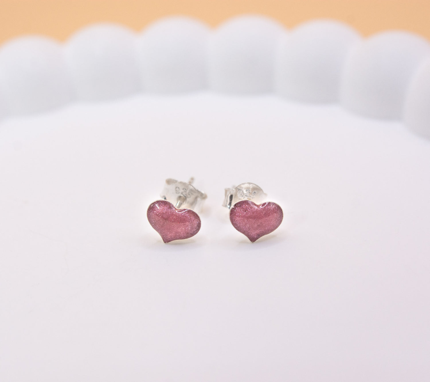 A close up shot of a pair of 925 sterling silver, pink coloured heart shaped stud earrings, containing cremation ashes