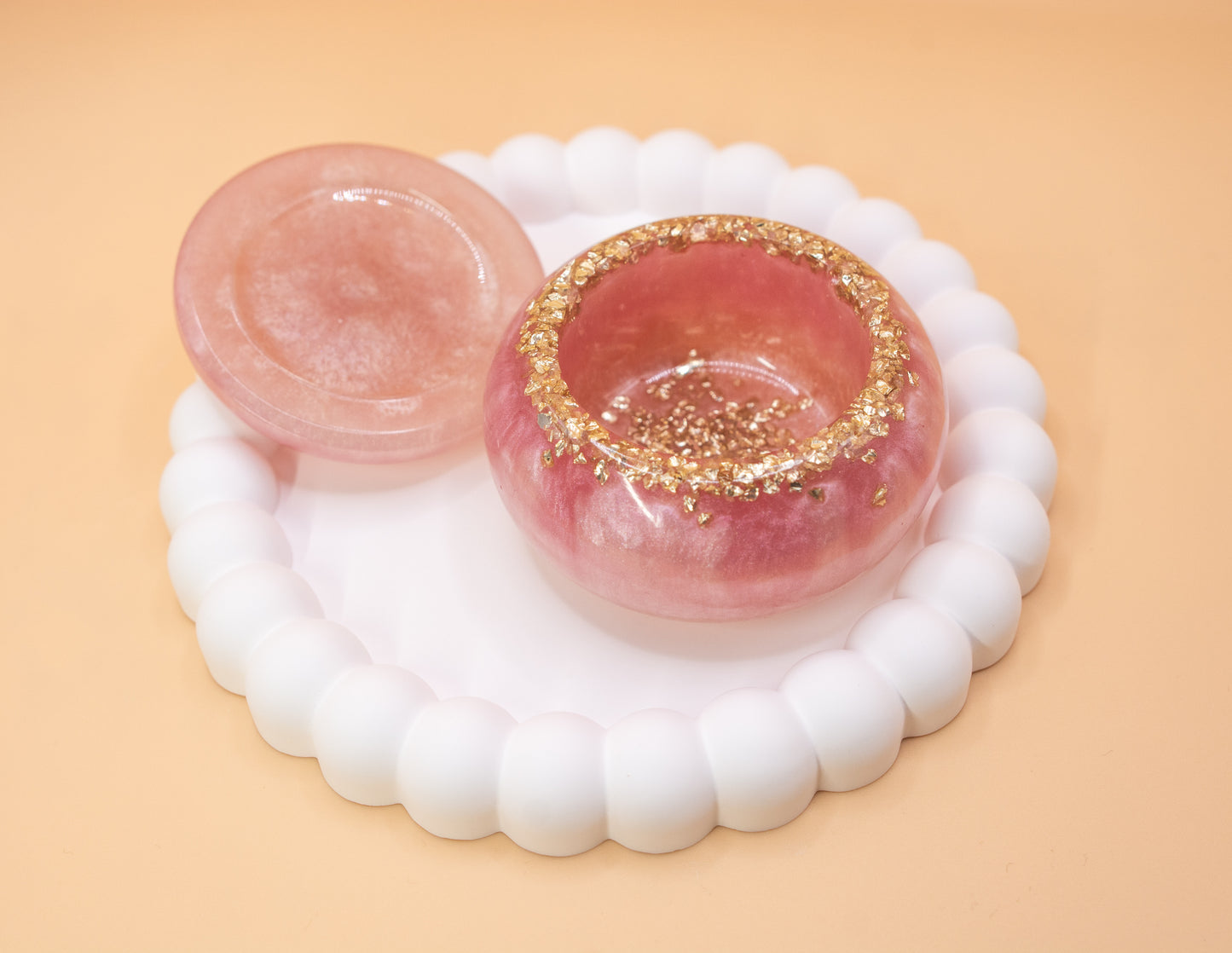 A front view of a metallic pearl pink handmade trinket pot, which has gold sparkle fragments in it, the lid is to the side of the pot