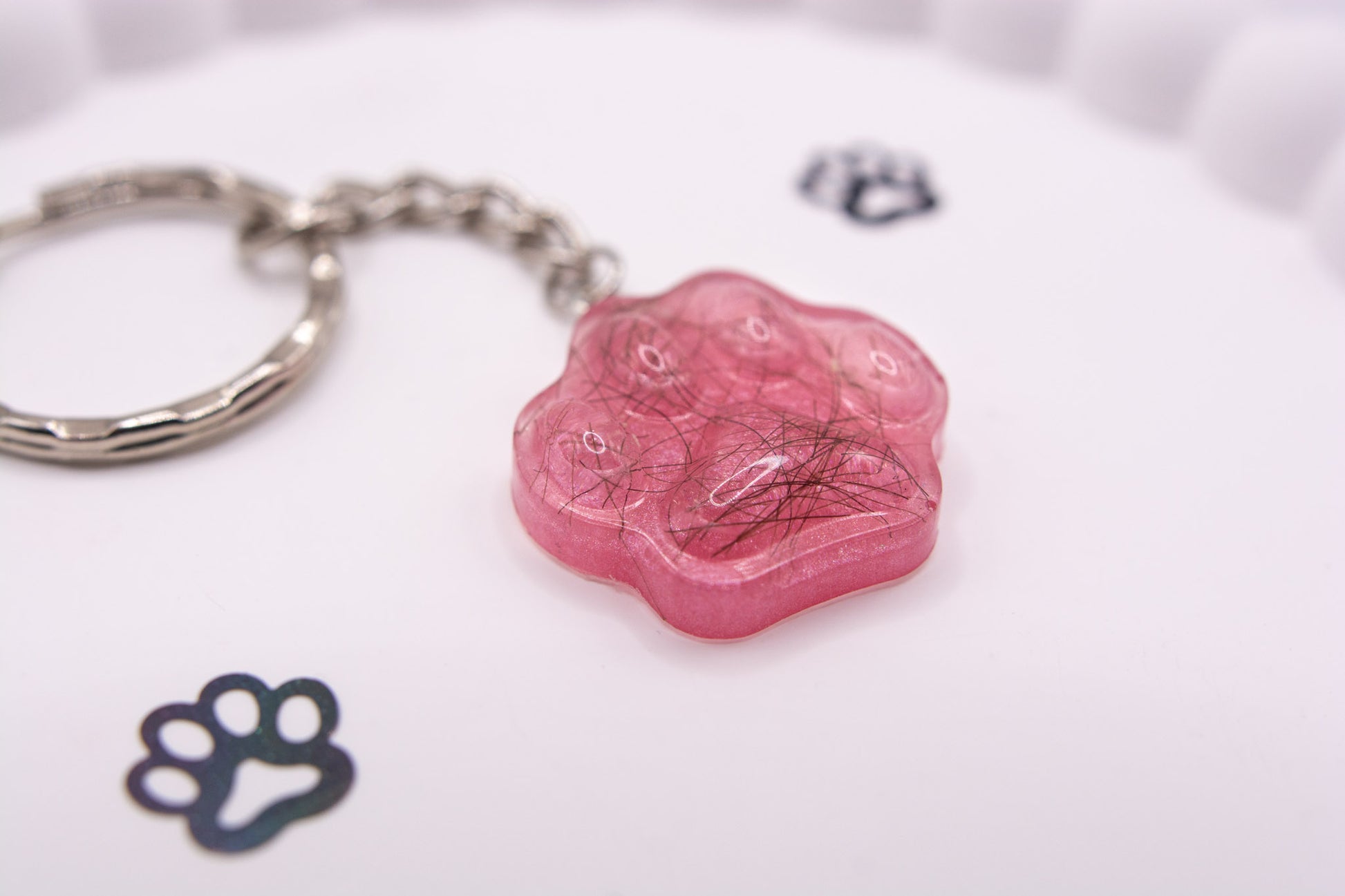 A close up angled view of a pink paw print shaped keepsake memorial keyring containing pet fur hair, set on a silver keychain