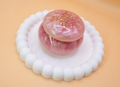 An angled view of a metallic pearl pink handmade trinket pot, which has gold sparkle fragments in it
