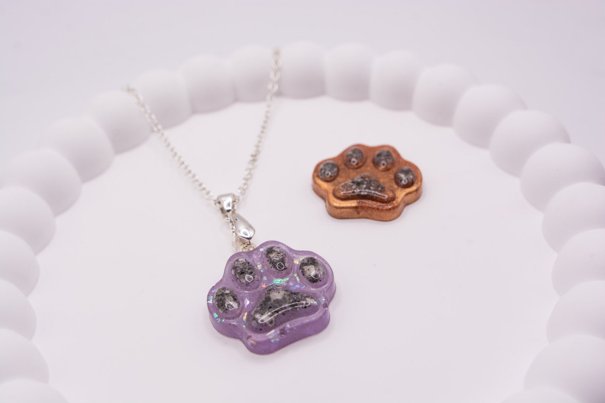 Angled view of one purple glitter and one metallic brown paw print keepsake memorial containing pet cremation ashes