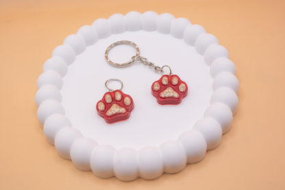 A white display tray, presenting two red paw prints, both containing lost pet dog cremation ashes. one is shown as a keying and the other is a tag for a dog collar.